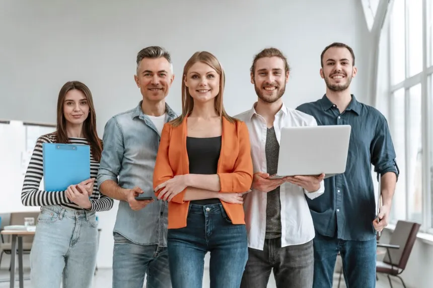 Five smiling coworkers stand with laptop and clipboard ready to get more customers after listing in our business directory